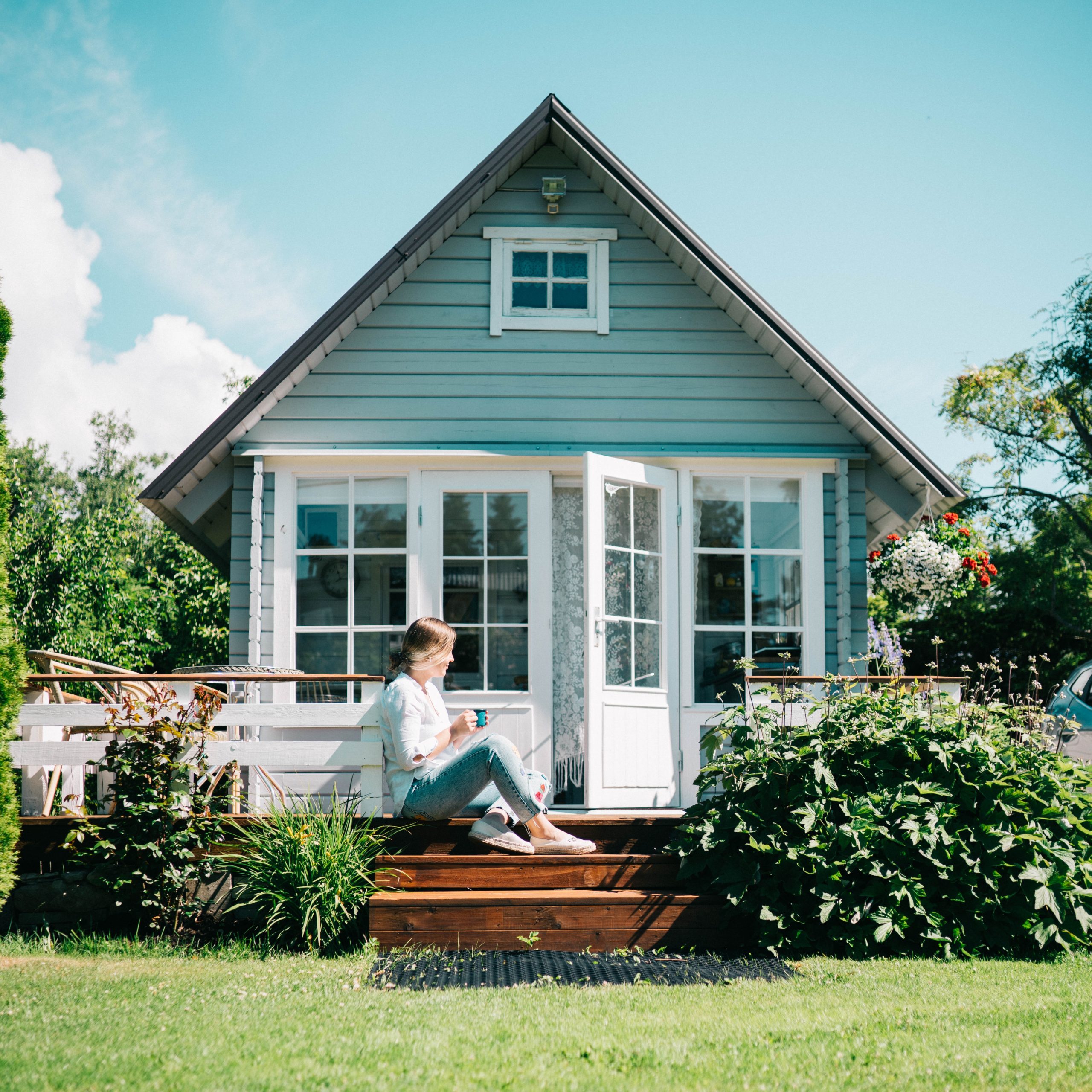 girl sitting on step of small blue house with white trim