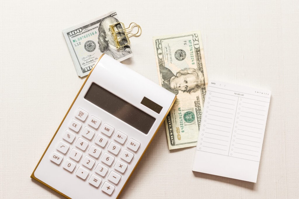 A calculator, folded wad of money and notepad laid out on a desk