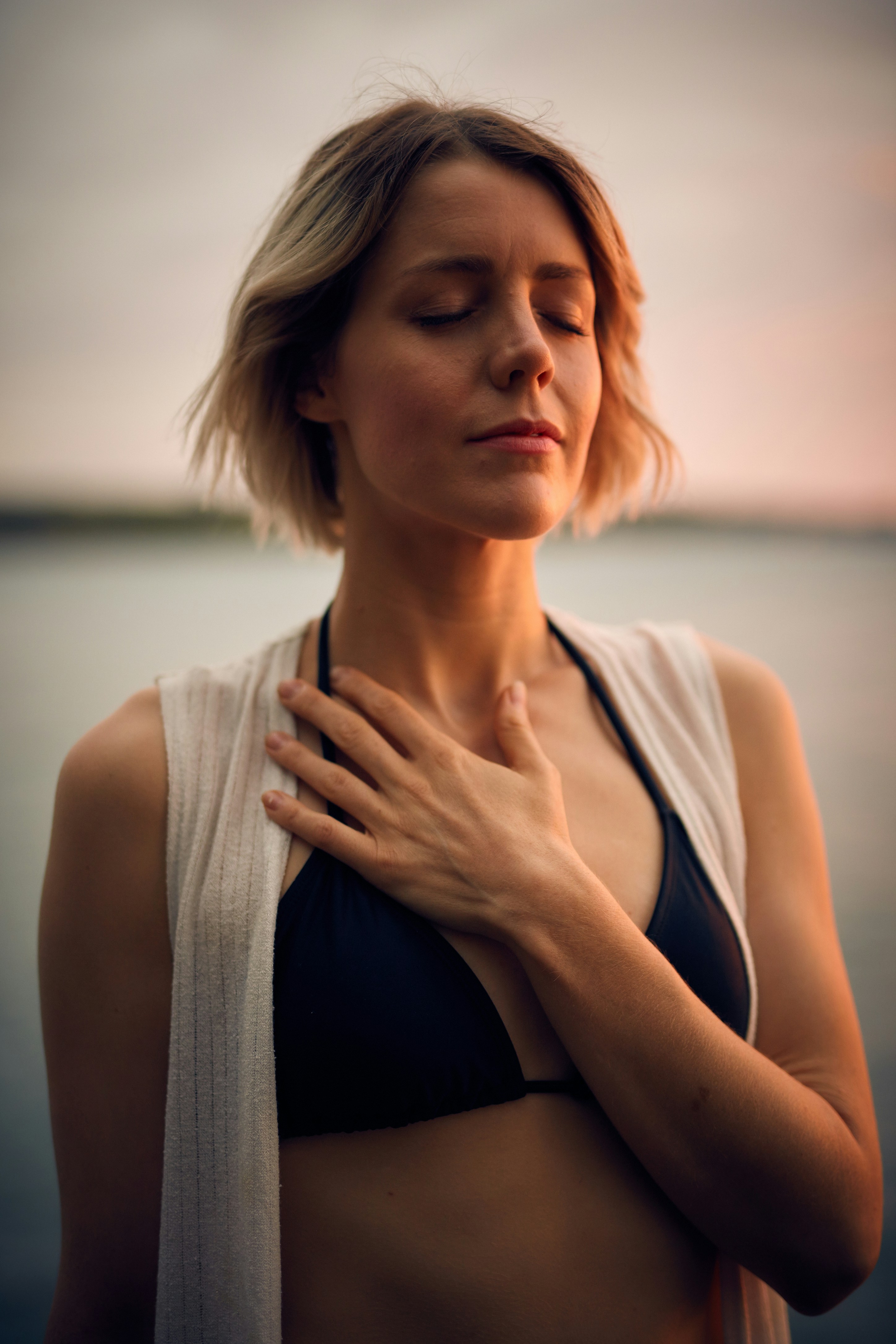 woman in black bikini and white sweater visualizing her goals with hand on chest